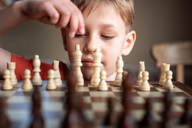 Young white child playing a game of chess on large chess board Chess board on table in front of school boy thinking of next move