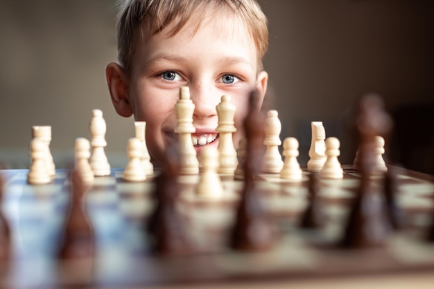 Young white child playing a game of chess on large chess board Chess board on table in front of school boy thinking of next move