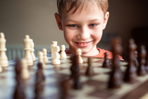 Young white child playing a game of chess on large chess board Chess board on table in front of school boy thinking of next move