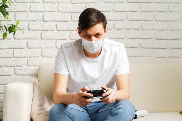 Young white man playing video games with medical mask on his face