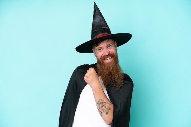 Young wizard in halloween isolated on blue background celebrating a victory