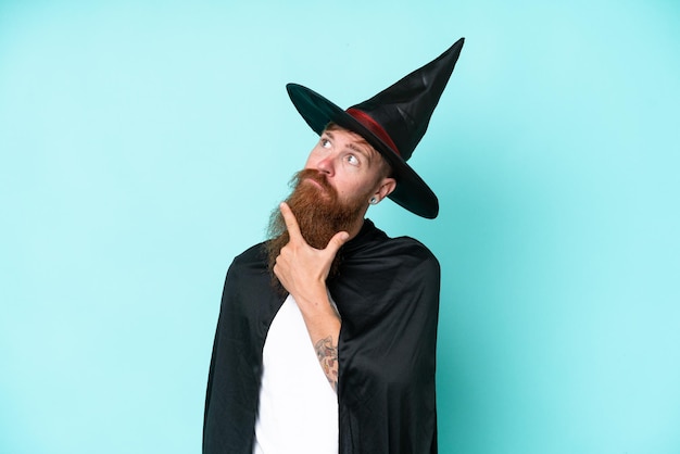 Young wizard in halloween isolated on blue background having doubts