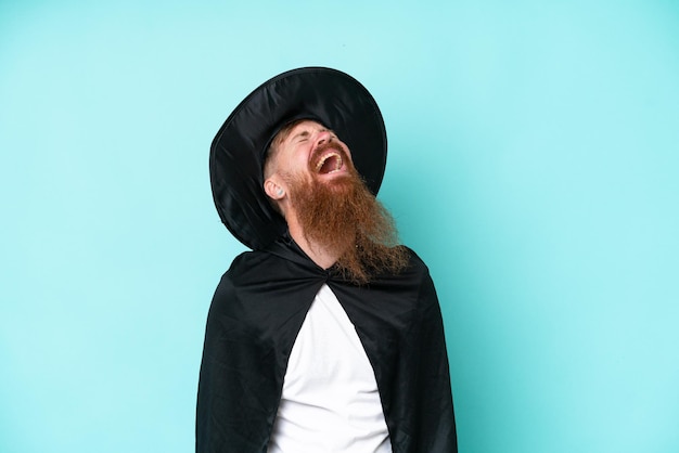 Young wizard in halloween isolated on blue background laughing