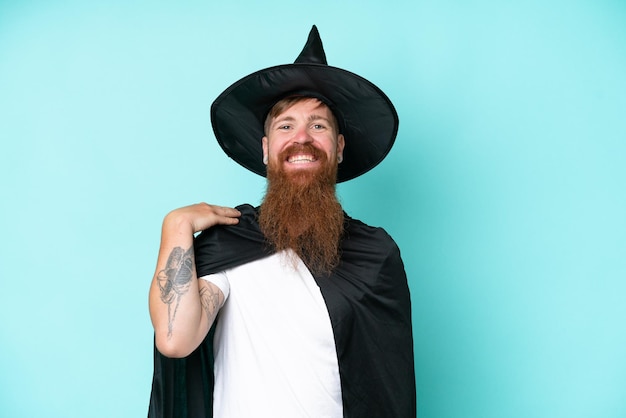 Photo young wizard in halloween isolated on blue background laughing