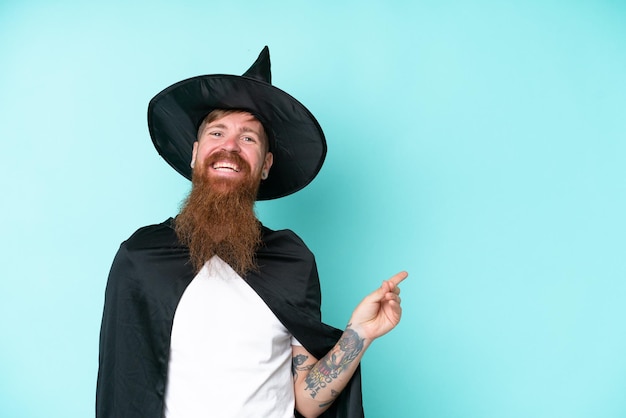 Young wizard in halloween isolated on blue background pointing finger to the side