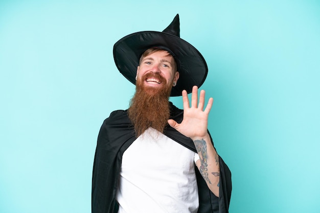 Photo young wizard in halloween isolated on blue background saluting with hand with happy expression