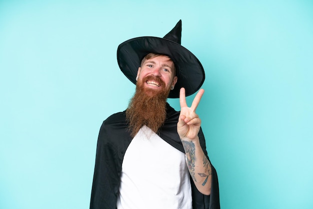 Photo young wizard in halloween isolated on blue background smiling and showing victory sign