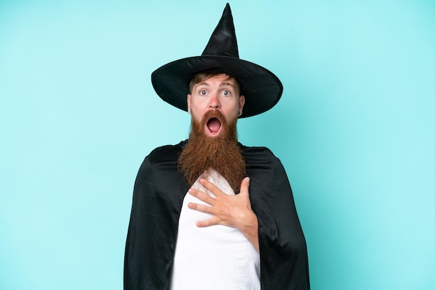 Young wizard in halloween isolated on blue background surprised and shocked while looking right