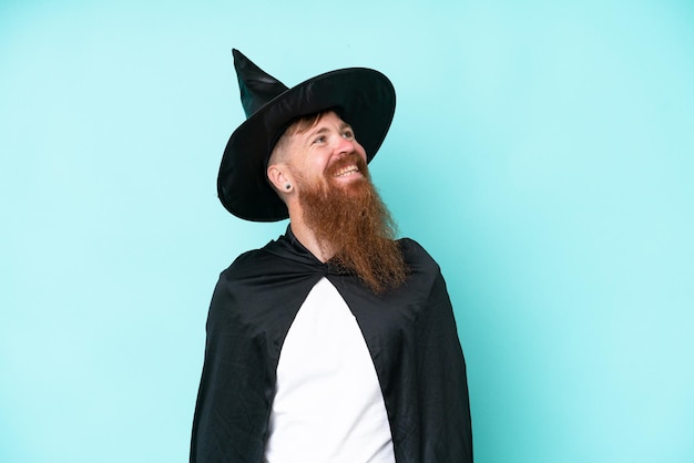 Young wizard in halloween isolated on blue background thinking an idea while looking up