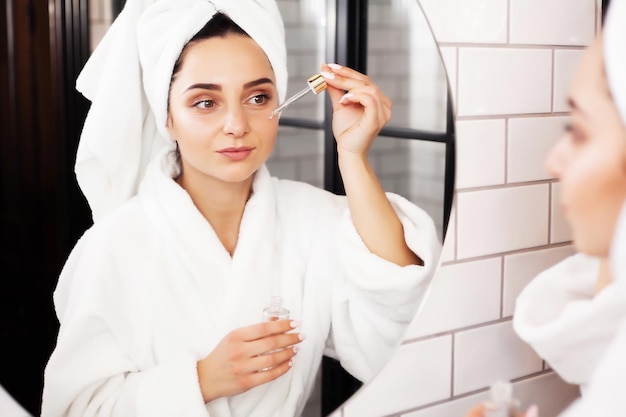 Young woman after shower going to apply skincare product, oil or serum.