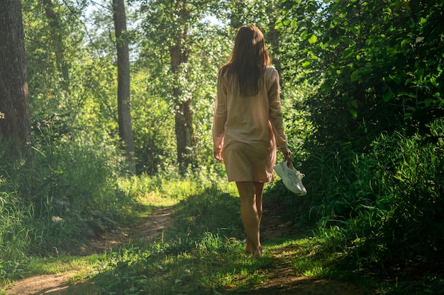 Young woman after swimming in the river walks along the forest road barefoot