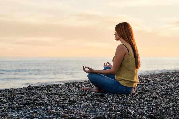 Young woman alone sitting on beach sand at sunset. Concept of relaxation and meditation