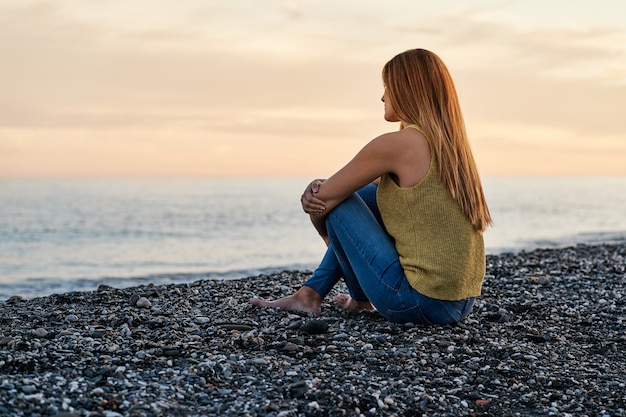 Young woman alone sitting on beach sand at sunset. Concept of relaxation and meditation