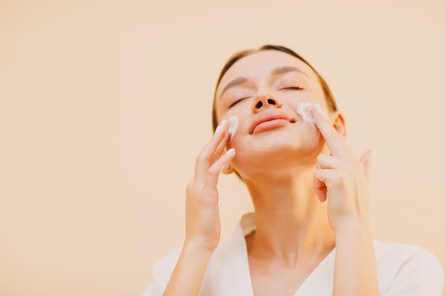 Young woman applying cosmetic white cream on her face