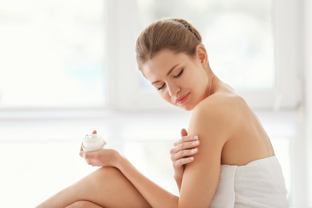 Photo young woman applying cream onto her skin on blurred background