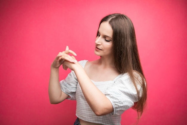 Young woman applying hand cream on pink background