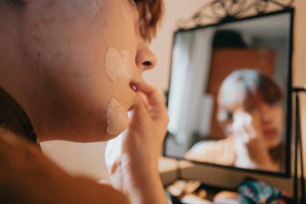 Young woman applying liquid foundation doing make up base at home getting ready and beauty. Looks in the mirror, paints her eyes with black eyeliner. Close-up