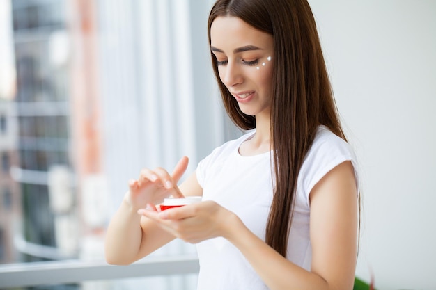 Young woman applying makeup on face at home