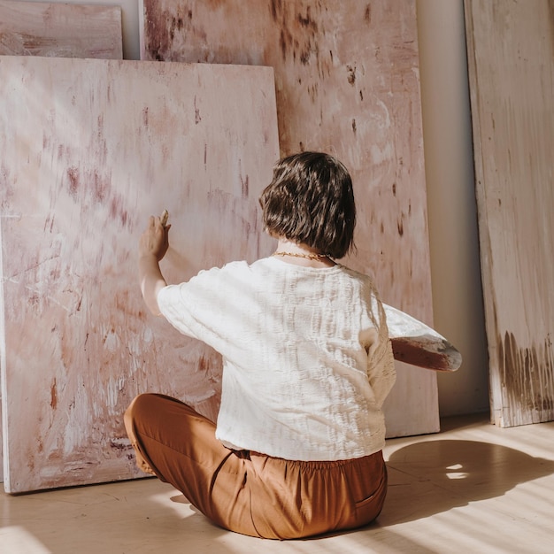 Young woman artist painting abstract picture in studio with sun light Aesthetic minimalist art work creation concept