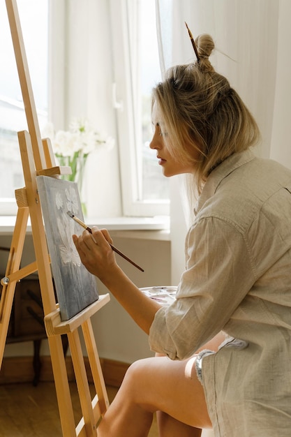 Young woman artist painting on canvas on the easel at home studio