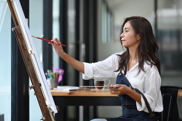 Young woman artist painting picture on canvas with water colors in her workshop.