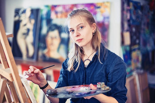 Young Woman Artist Working On Painting In Studio.