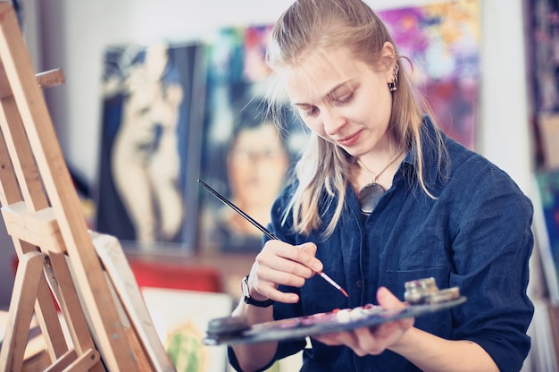 Young Woman Artist Working On Painting In Studio.