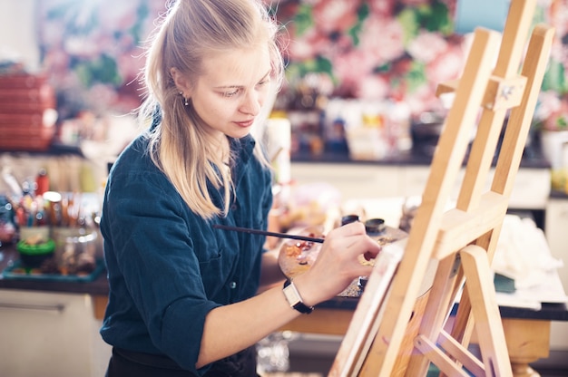 Young Woman Artist Working On Painting In Studio.