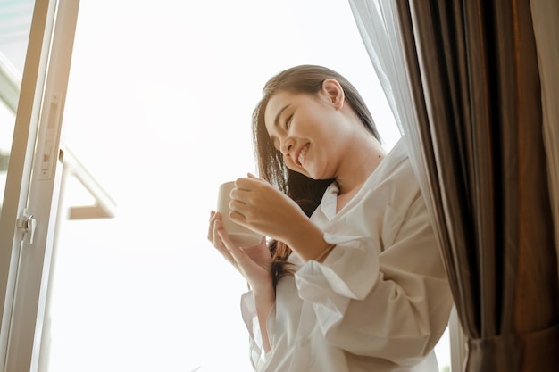 Young woman asia living at home relaxing and drinking cup of hot coffee in the bedroom on holiday. Asian, asia, relax, alone, technology, lifestyle concept.