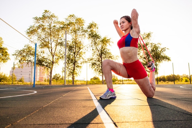 Young woman athlete with an amputated arm and burns on her body limber up on the sports field Resistance band exercise outdoor at sunset