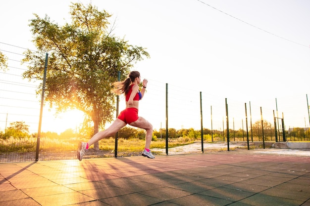 Young woman athlete with an amputated arm and burns on her body runs around the sports field She sprints a short distance outdoors at sunset