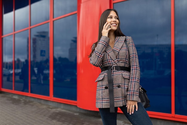 A young woman in an autumn coat speaks on a mobile phone against the background of a red blue