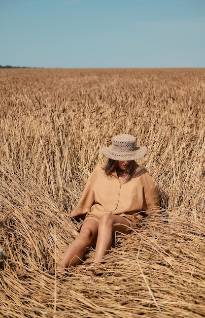 Young woman barefoot in linen clothes and a hat on a background of dry grass romantic girl in a hat