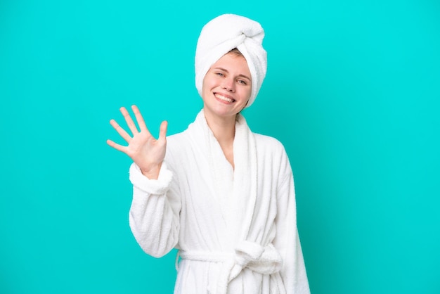 Young woman in a bathrobe isolated on blue background counting five with fingers