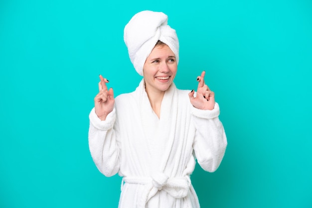 Young woman in a bathrobe isolated on blue background with fingers crossing