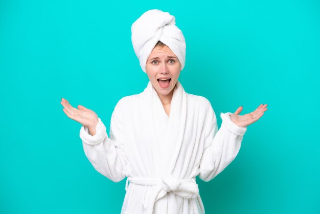 Young woman in a bathrobe isolated on blue background with shocked facial expression