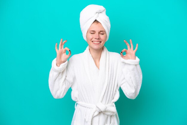 Young woman in a bathrobe isolated on blue background in zen pose