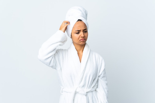 Young woman in bathrobe isolated having doubts while scratching head