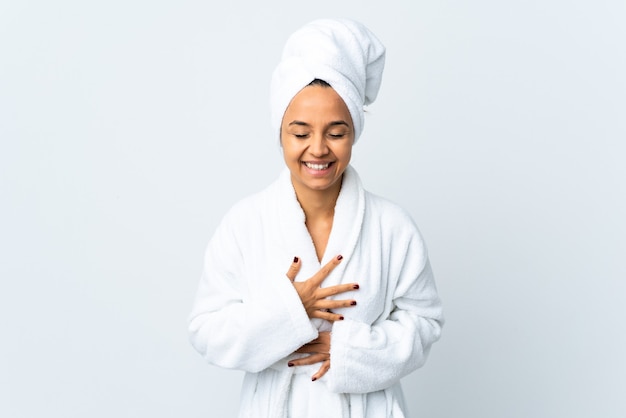 Young woman in bathrobe over isolated white wall smiling a lot