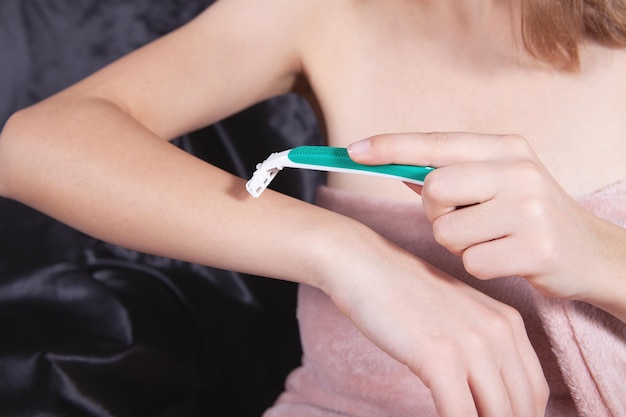 Young woman in bathrobe shaving her hand