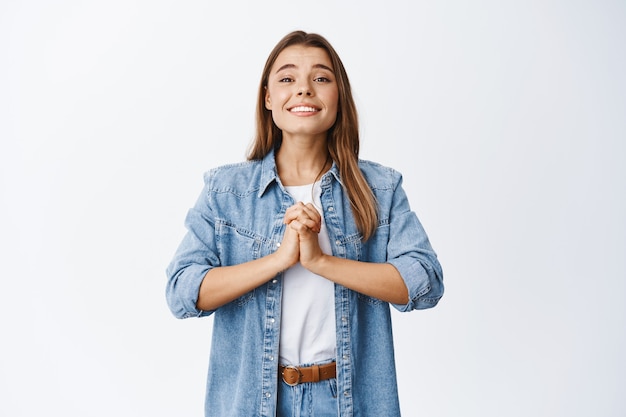 Young woman begging for help, need something from you and clinging, standing against white wall