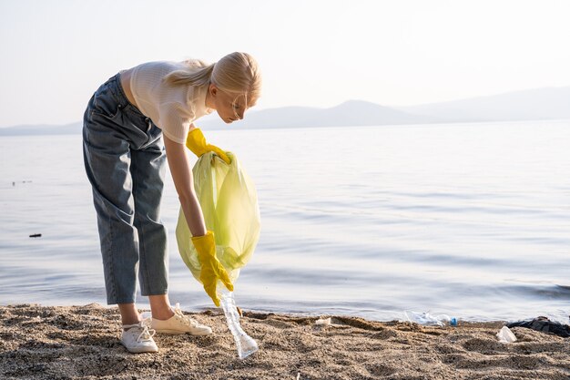 Photo a young woman bent down and picks up an empty plastic bottle to put it in the trash bag. conservation of nature and respect for the planet.