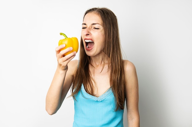 Young woman biting whole fresh yellow paprika on white background