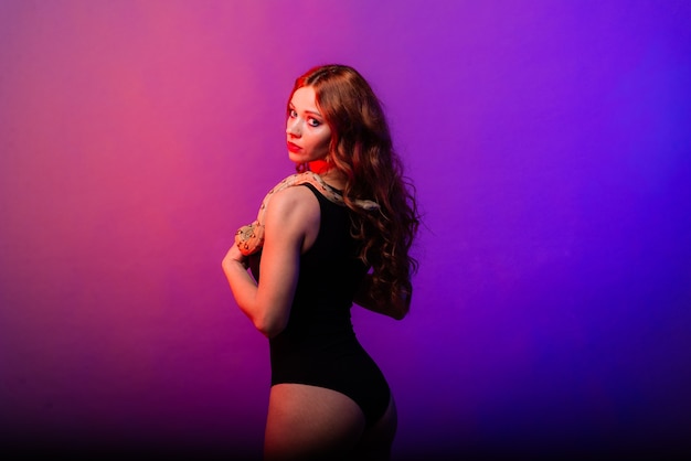 Young woman in a black bikini posing with python against abstract  background