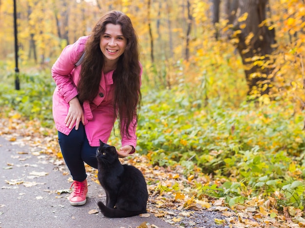 Young woman and a black cat in the autumn park