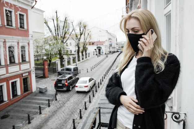 A young woman in a black mask is standing on the balcony of the office and talking on the phone