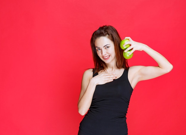 Young woman in black singlet holding green apples and pointing at herself