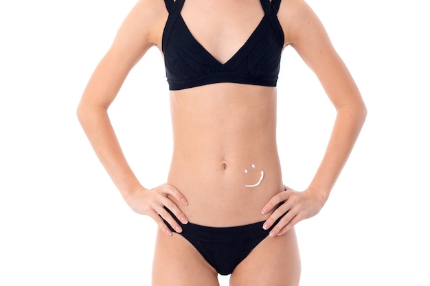 Young woman in black swimsuit and skin protector cream on her belly isolated on white wall