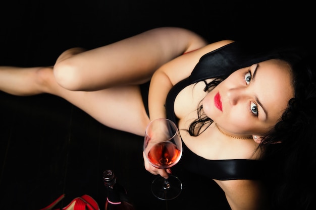 young woman in black underwear holding a glass of red wine