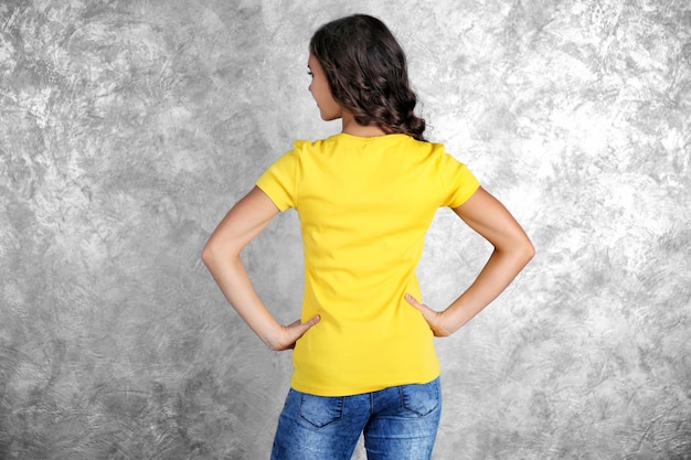 Young woman in blank yellow tshirt standing against grey textured wall